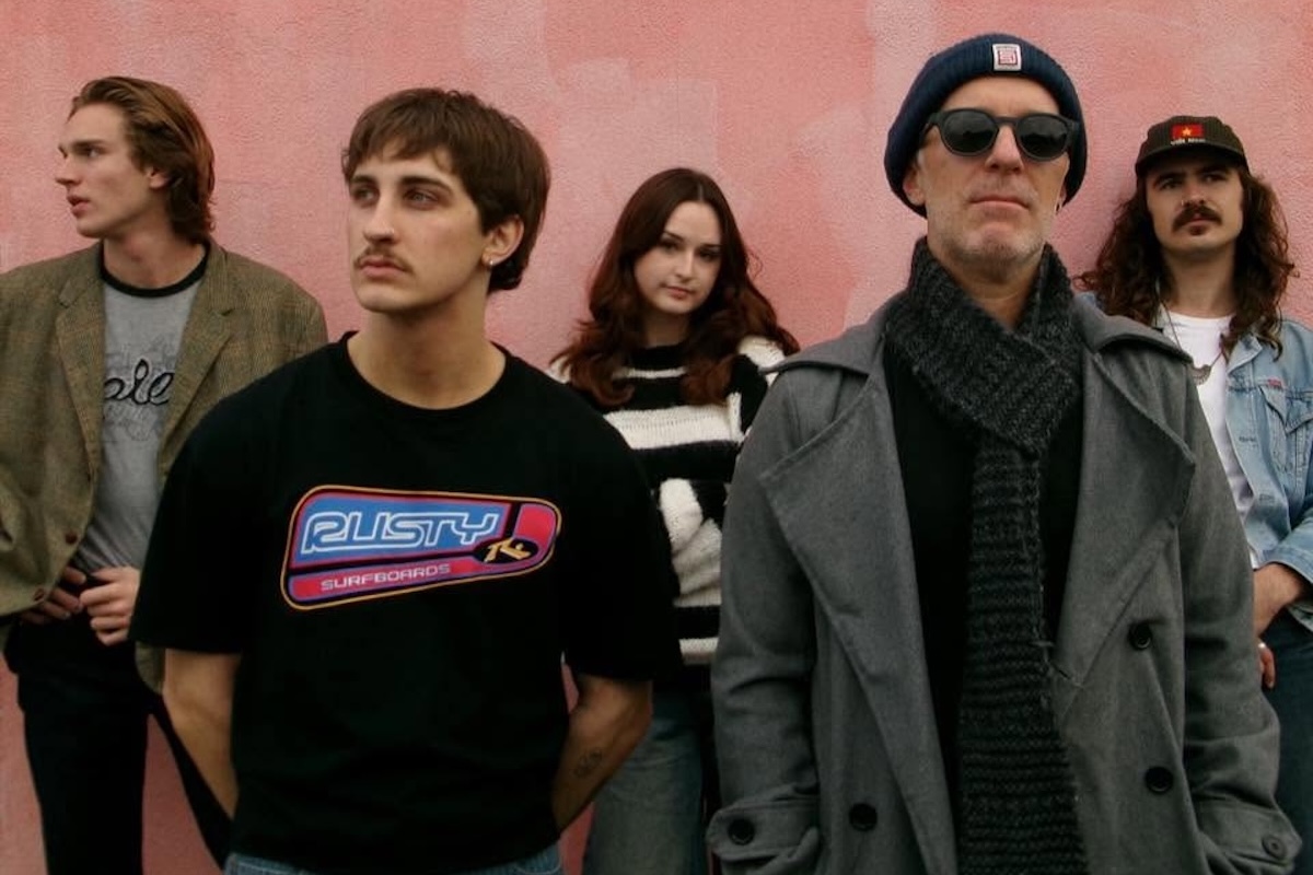 Promotional band photo of indie rock group The Hazys standing outdoors together against a textured pink wall.